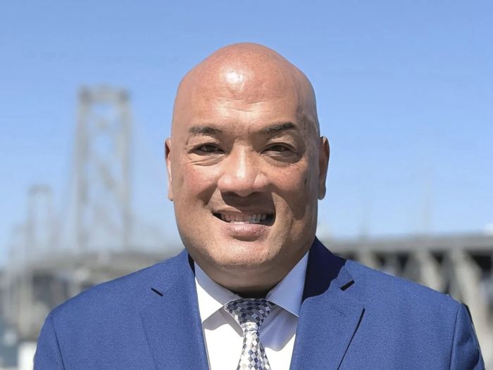 Louis Wong smiling outdoors with the Bay Bridge in the background