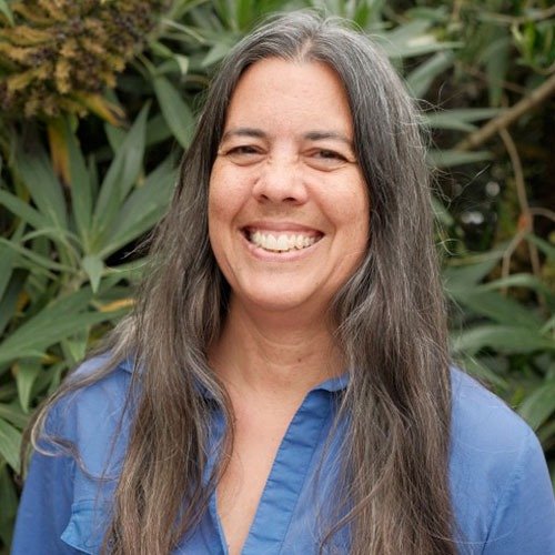 Supryia Ray smiling outdoors in front of green foliage